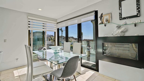 Un comedor moderno con una mesa y sillas de vidrio, chimenea y vistas amplias a través de grandes ventanales.