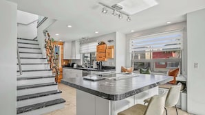 Una cocina moderna con una isla central, una escalera y un ventanal grande.