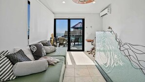 Un salón moderno con un sofá, una mesa de vidrio y vistas al mar a través de un ventanal corredero.