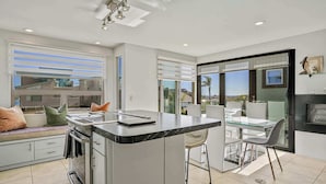 Una cocina moderna con una isla central, un comedor con mesa de vidrio y vista al exterior.