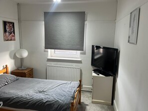 Um quarto com uma cama, uma mesa de cabeceira com luminária, uma TV e um radiador.
