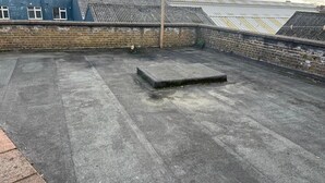 Una azotea con superficie de concreto, una pequeña plataforma de concreto y un muro de ladrillo con ventanas.