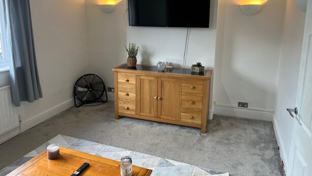 Una sala de estar con un aparador de madera, un televisor de pantalla plana y dos luces fijadas a la pared.