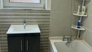 Un baño con lavamanos blanco, armarios negros, bañera y ventana.