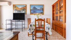 Un comedor con una mesa preparada para cuatro, un televisor y un aparador con puertas de vidrio.