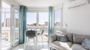 Una sala de estar moderna con un sofá, una mesa de comedor con sillas y ventanas amplias con cortinas.