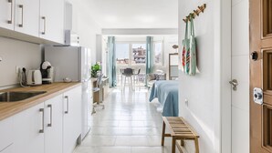 Cocina moderna con armarios blancos y encimera de madera, que da paso a un comedor con mesa y sillas.