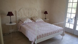 A bedroom with a white metal bed frame, two bedside tables with lamps, and a large window. - Villa les Carlets (Saignon)