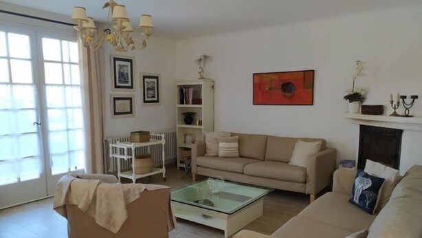 A living room with a beige sofa, a glass coffee table, a white side table, and a bookshelf. - Villa les Carlets (Saignon)