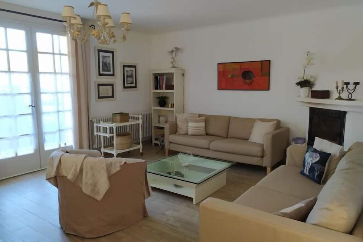 A living room with a beige sofa, a glass coffee table, a white side table, and a bookshelf.
