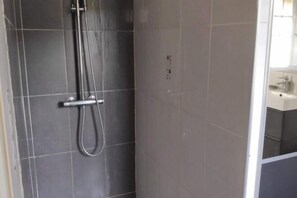 A bathroom with dark tiles, a shower, and a visible sink with a mirror. - Villa les Carlets (Saignon)