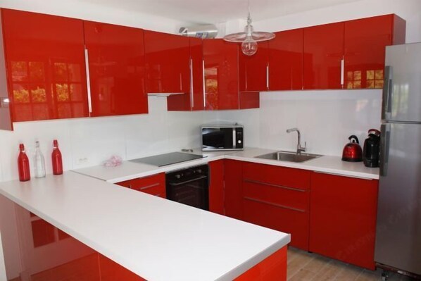 A modern kitchen with red cabinets, a white countertop, a microwave, a sink, and a kettle. - Villa les Carlets (Saignon)
