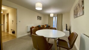 A dining area with a round table and four chairs, a sofa with cushions, a radiator, and a painting on the wall.