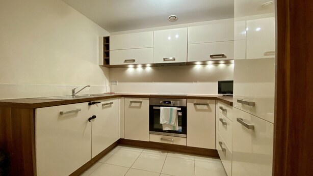 A modern kitchen with white cabinets, a built-in oven, and a stainless steel sink.