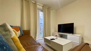 A modern living room with a brown leather sofa, a white coffee table, and a flat-screen TV on a white stand.