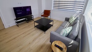 Ein modernes Wohnzimmer mit einem Flachbildfernseher, einem schwarzen Couchtisch, einem grauen Sofa, einem Holznachttisch und einem roten Sessel.