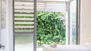 A bedroom with a checkered bedspread, a rolled towel on the bed, and a view of greenery through a glass door. - Zinc One Select - Oceanstays - ocean views (Yamba)