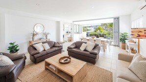 A spacious living room with two brown leather sofas, a wooden coffee table, and a view of the outdoor patio area. - Zinc One Select - Oceanstays - ocean views (Yamba)
