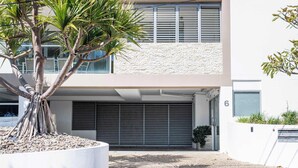 A modern building with a garage door, a tree in a planter, and a stone wall. - Zinc One Select - Oceanstays - ocean views (Yamba)