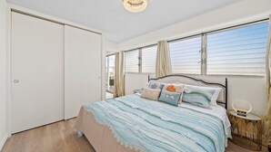 A bedroom with a bed, a nightstand, a clock, and a window with curtains.
