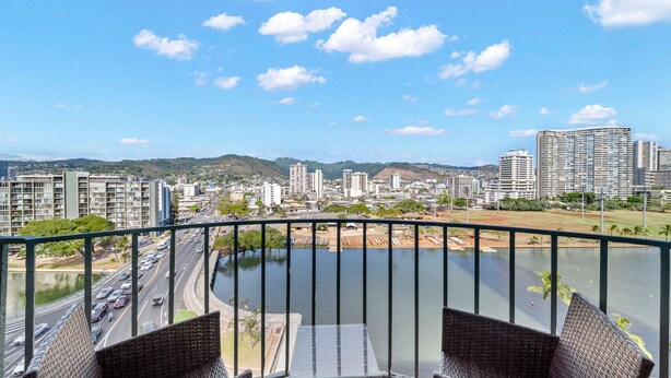 A balcony with wicker furniture overlooking a cityscape, a river, and a road with vehicles.