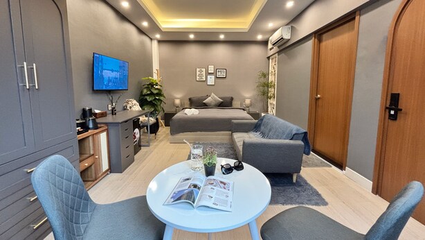 A modern bedroom with a bed, bedside tables, a TV, and a seating area with a table and chairs. - AMANA Hotel & Residence - Vo Thi Sau (Ho Chi Minh City)
