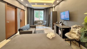 A modern hotel room with a bed, a desk, a chair, a TV, and a view of the outdoors. - AMANA Hotel & Residence - Vo Thi Sau (Ho Chi Minh City)