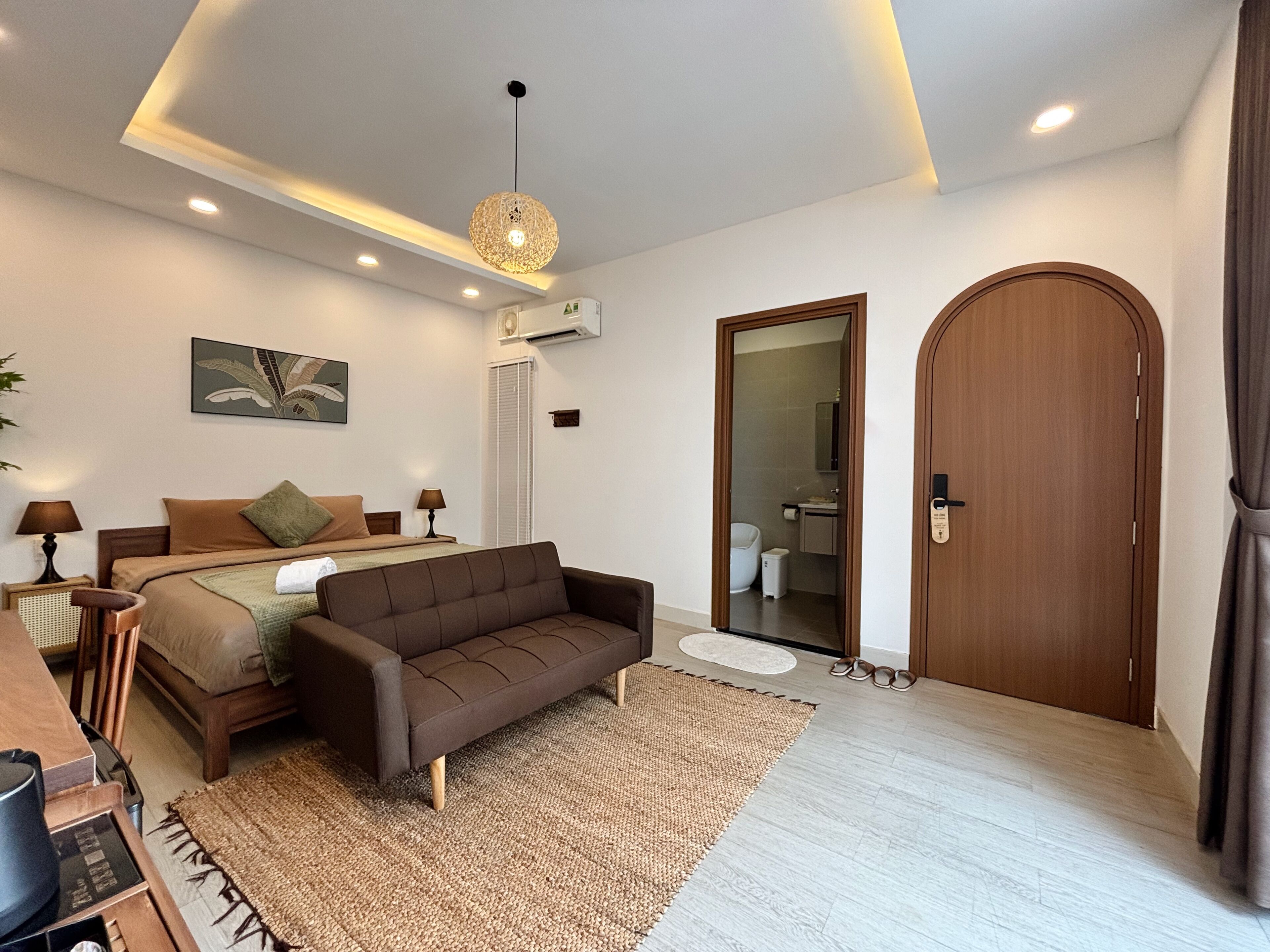 A modern bedroom with a bed, a brown sofa, a rug, and a wooden door.