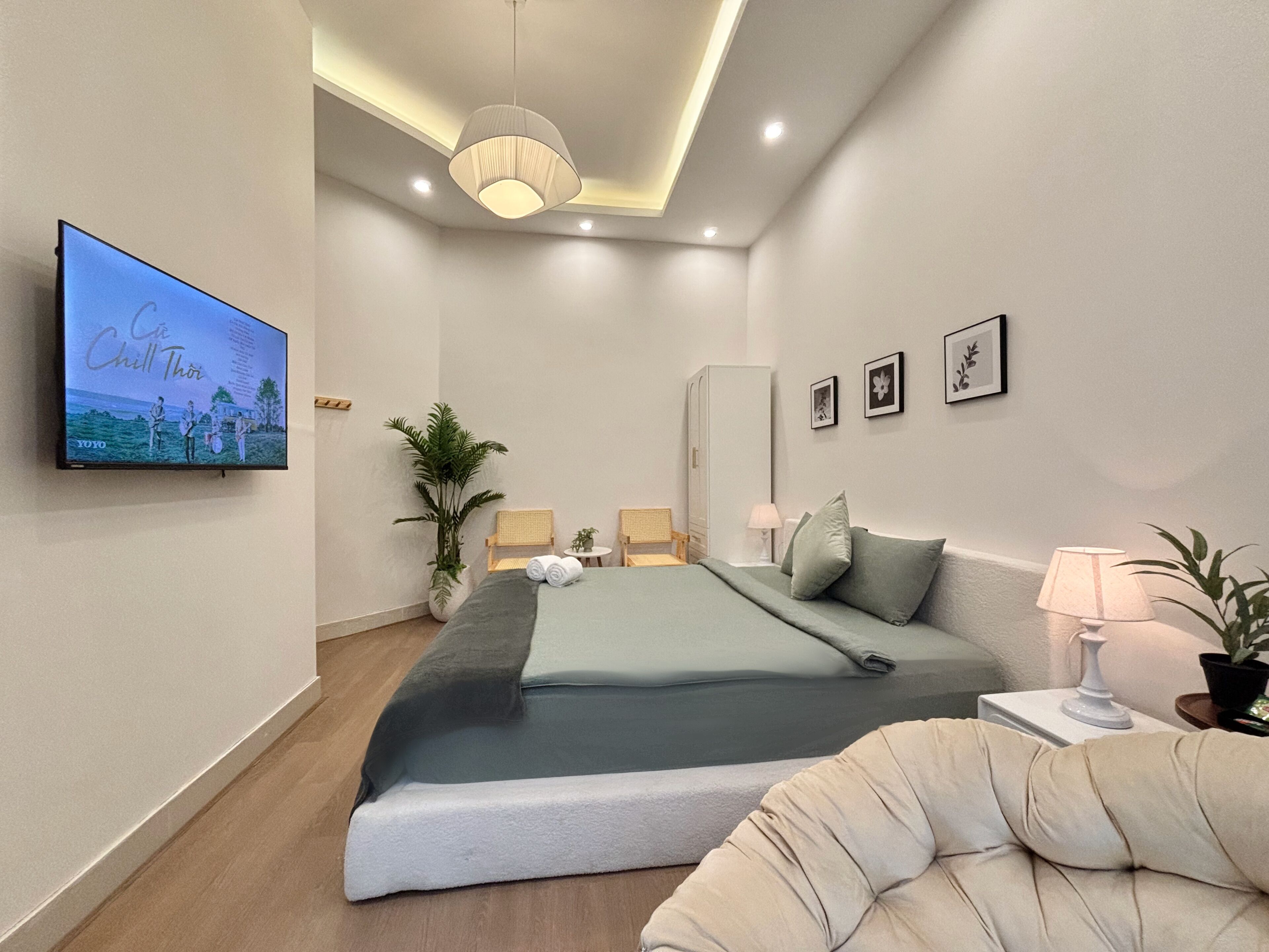 Un dormitorio moderno con cama, televisor en la pared, una planta y una silla.