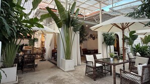 A spacious indoor area with high ceilings, large windows, and abundant greenery. There are wicker furniture and a central table with chairs. - AMANA Hotel & Residence - Vo Thi Sau (Ho Chi Minh City)