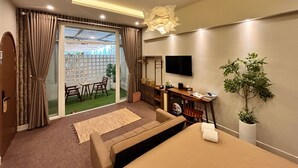 A modern hotel room with a sofa, a desk, a TV, and a potted plant. - AMANA Hotel & Residence - Vo Thi Sau (Ho Chi Minh City)
