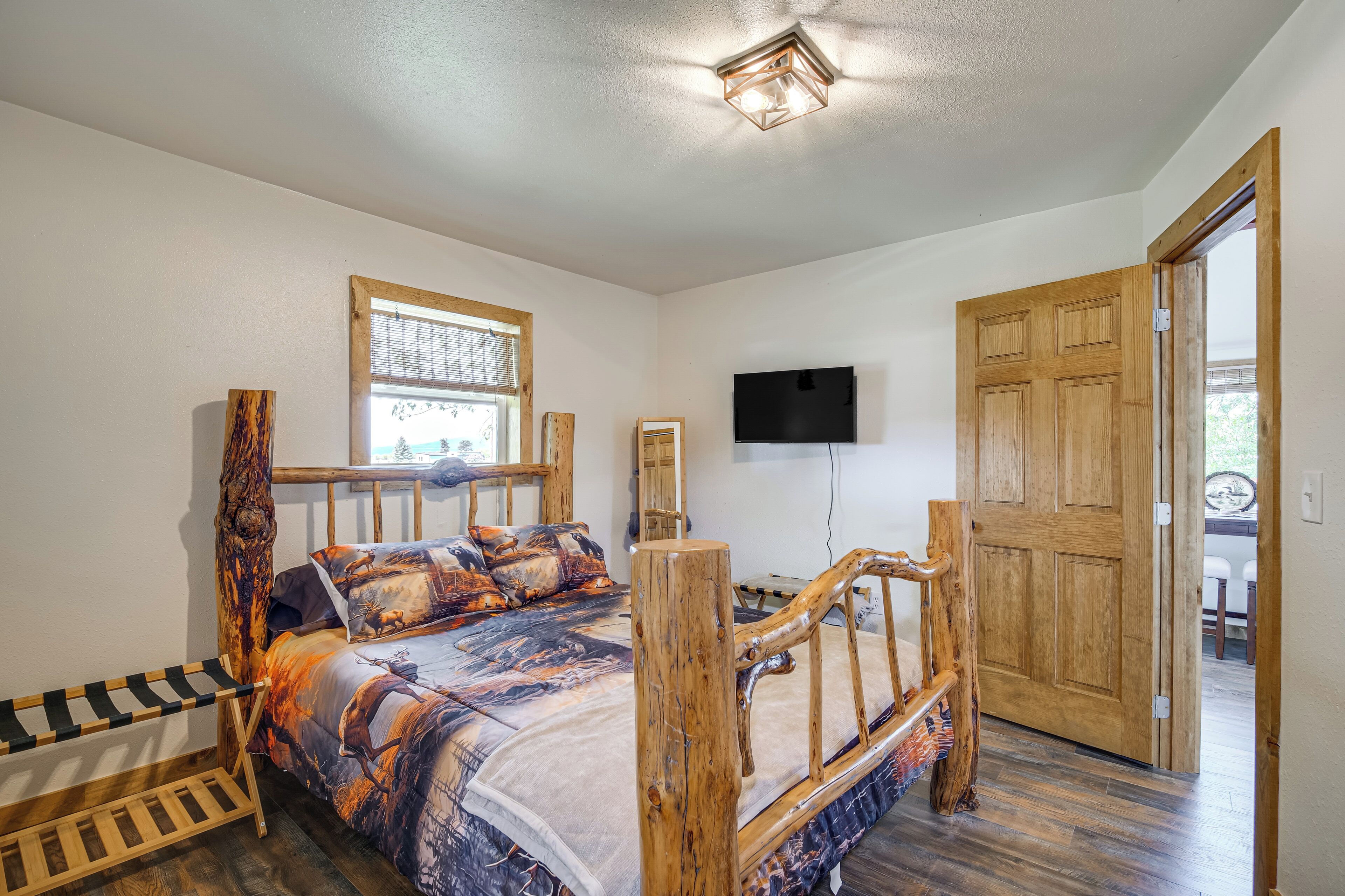 Ein Schlafzimmer mit einem Holzbettgestell, einer Bank, einem an der Wand befestigten Fernseher und einer Holztür.