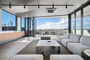 Un espace de vie extérieur moderne, doté d’un canapé, de fauteuils et d’une table, avec de grandes fenêtres offrant une vue sur le ciel.