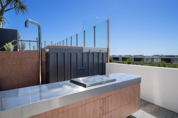 A modern outdoor kitchen area with a stainless steel countertop and wooden cabinetry.