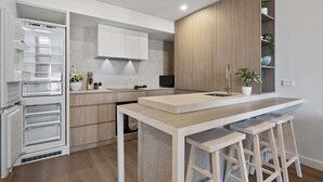 Una cuina moderna amb frigorífic integrat, armaris de fusta, una illa central amb tamborets i microones.