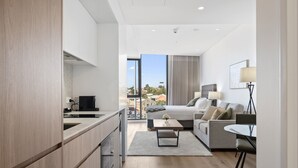 A modern hotel room with a kitchenette, a bed with a view, a seating area, and a dining table. - Bright Studio in Trendy North Fremantle (North Fremantle)