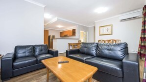 Un salon avec deux canapés en cuir noir, une table basse en bois et un coin repas comprenant des chaises et une table en bois.