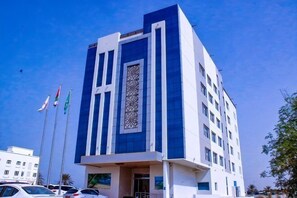 A modern building with a prominent vertical design, multiple windows, and a central decorative element. - Wave View Hotel (Seeb)