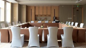 Un salón de conferencias con una larga mesa, sillas blancas y una decoración en tonos neutros.