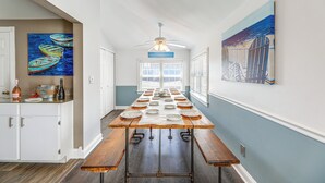 A long dining table set up in a hallway with white cabinets and artwork on the walls. - Steps to Shore: Newly Renovated Dewey Beach Home! (Dewey Beach)