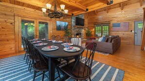 L’intérieur d’un chalet en bois comprend un coin repas, une cheminée, un canapé et un drapeau américain.