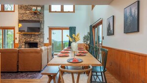 A dining area with a stone fireplace, wooden dining table, and chairs. - Sleeps 20! Hot Tub~Outdoor Theater~Fire Pit~Games (Fairview)
