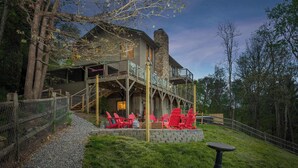 A rustic cabin with a stone chimney, a wooden deck, and red Adirondack chairs. - Sleeps 20! Hot Tub~Outdoor Theater~Fire Pit~Games (Fairview)