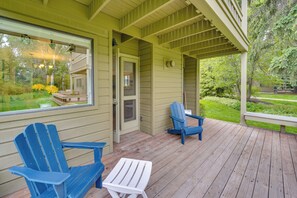 A covered porch with two Adirondack chairs and a small table.
