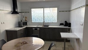 Une cuisine compacte avec une table de salle à manger ronde, des meubles de rangement sombres, un four à micro-ondes et une fenêtre à vitrage dépoli.