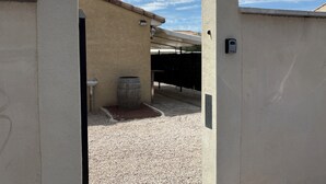 Un espace extérieur abrité, doté d’un sol en gravier, d’une barrique en bois et d’un appareil fixé au mur.