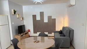 Un salon moderne avec une table ronde en bois, des chaises noires, un canapé gris et un panneau décoratif mural.