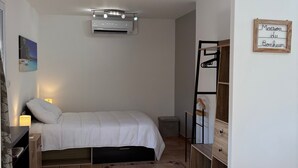 Une chambre à coucher comprenant un lit, une lampe de chevet, un appareil de climatisation et une armoire en bois.