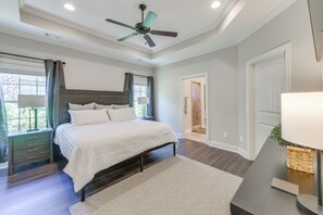 Relax in this serene bedroom with a large bed, nightstand, and dresser, complete with a ceiling fan and a window with curtains.