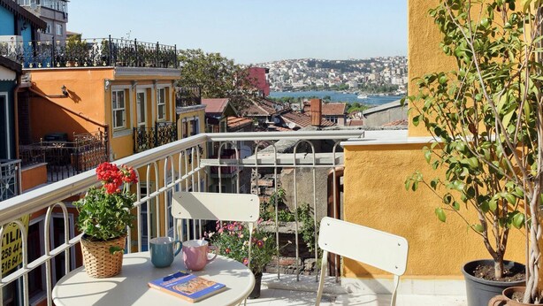 A balcony with a view of a cityscape, a table with chairs, and potted plants. - Charming 2-bedroom house with WiFi and AC in vibrant Istanbul (Unknown)